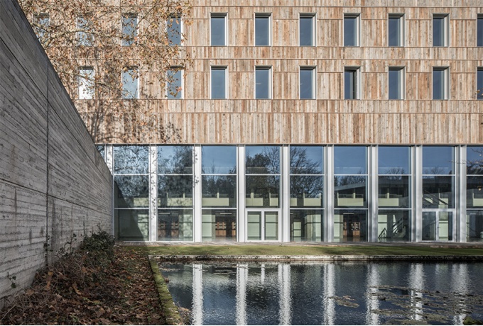 Façade principale, vue depuis le niveau bas de la partie enseignement du programme (R-1). La terrasse devant le bassin est réalisée en bois de réemploi (bois exotique récupéré sur des docks aux Pays-Bas).<br/> Crédit photo : Defourny Samuel