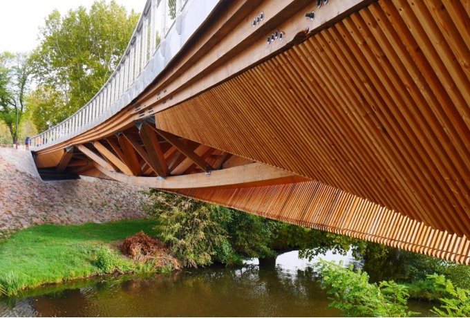 Vue du dessous, la passerelle revèle sa structure en mono poutre treillis à devers, supportant un tablier en CLT par l’intermédiaire d’une série de chevalets.